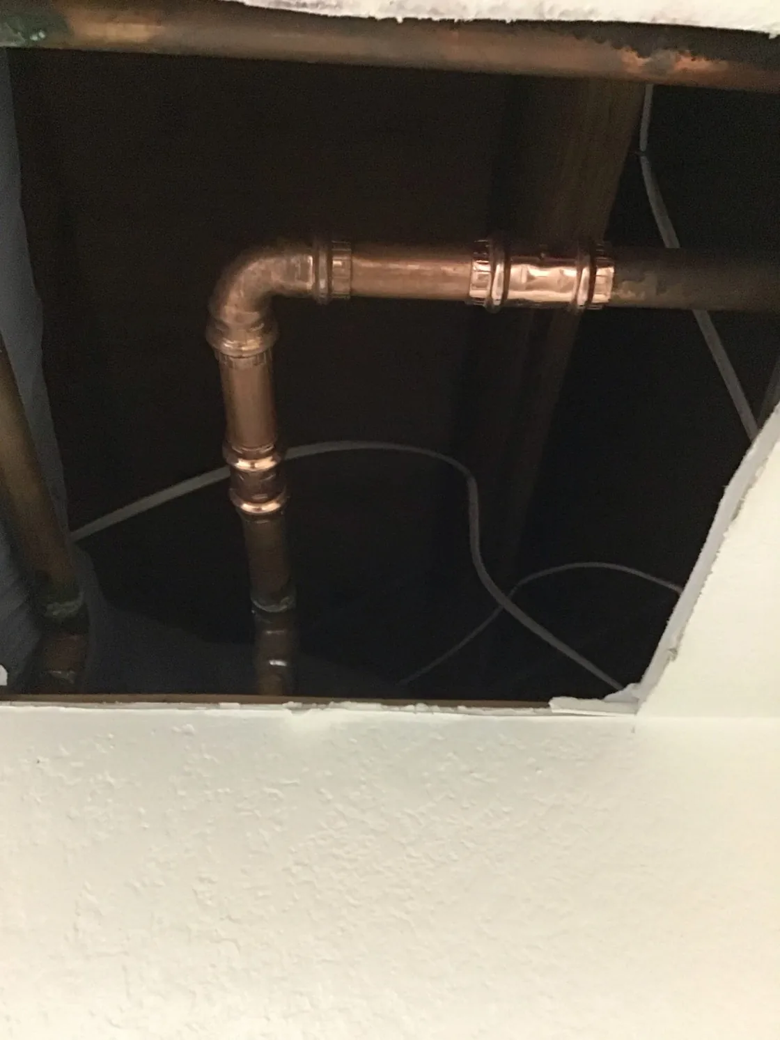 Repaired copper pipe visible through an opening in a ceiling