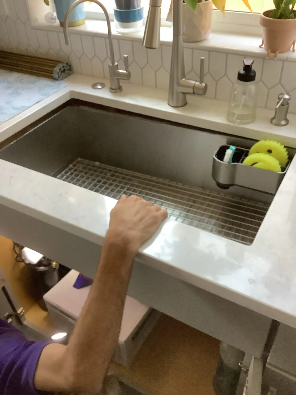 A Trident technician reaching beneath a stainless kitchen sink