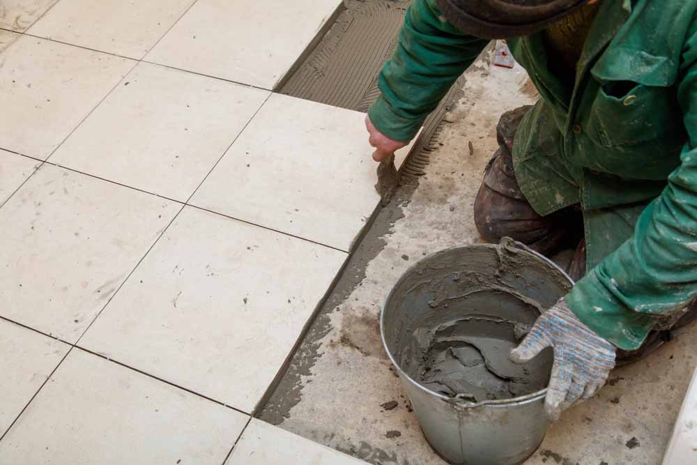 worker laying down tiles in bathroom
